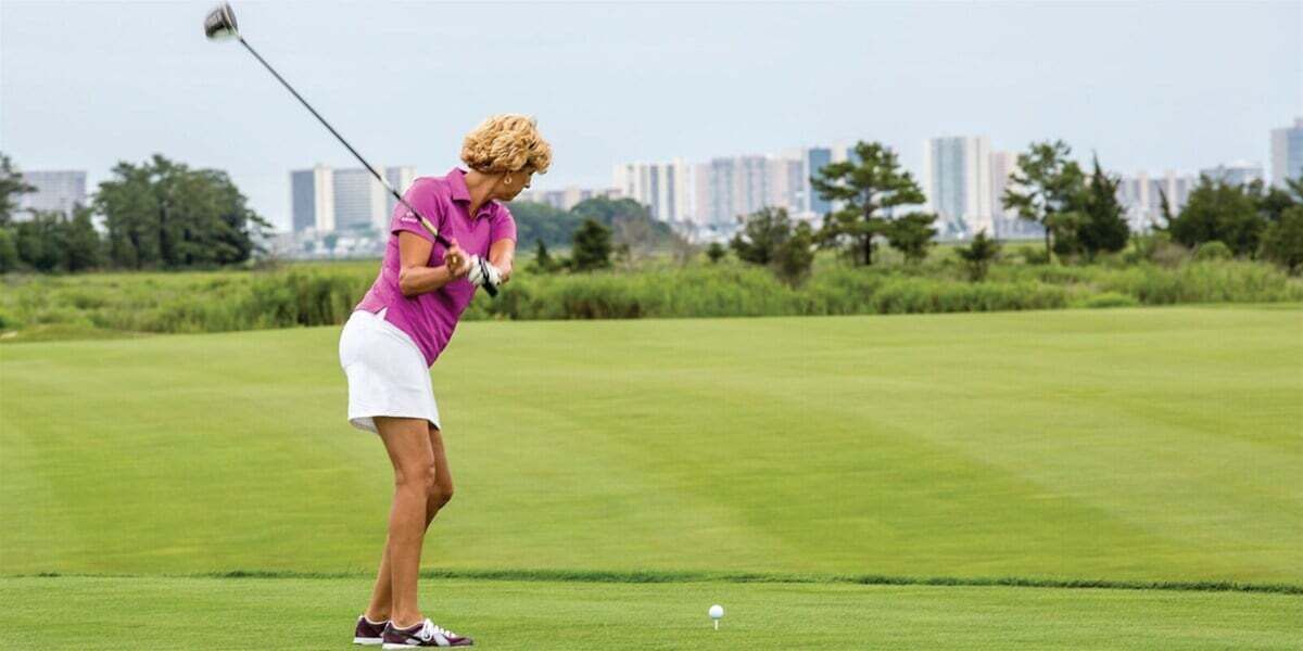A person playing golf on a green field with a city skyline in the background.