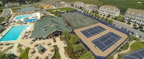 An aerial view of a resort with a swimming pool, tennis courts, and a building with a green roof.