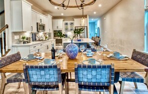 Uma sala de jantar com uma mesa de madeira posta para seis pessoas, rodeada por cadeiras estofadas em azul.