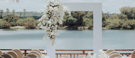 A wedding ceremony setup with a white aisle, chairs, and floral decorations against a lake backdrop.