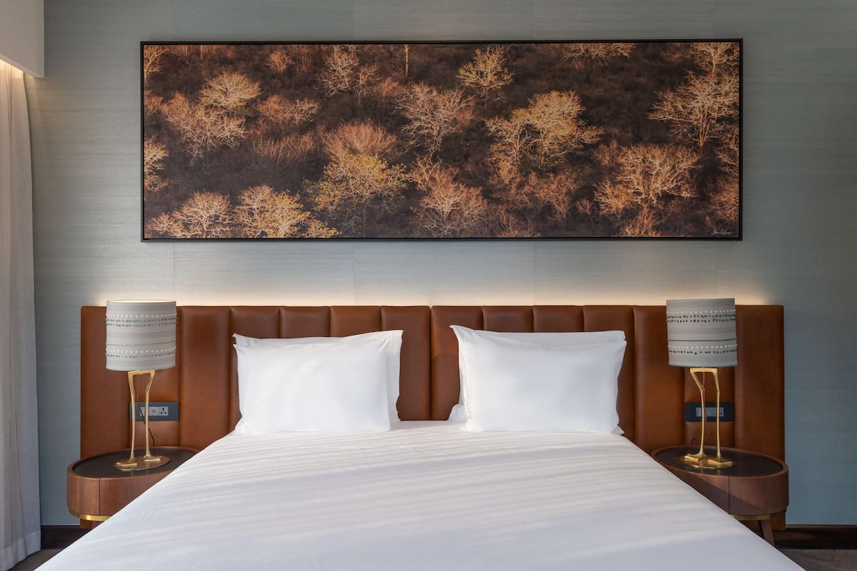 Une chambre d’hôtel avec un grand lit, deux tables de chevet et une œuvre d’art accrochée au mur.