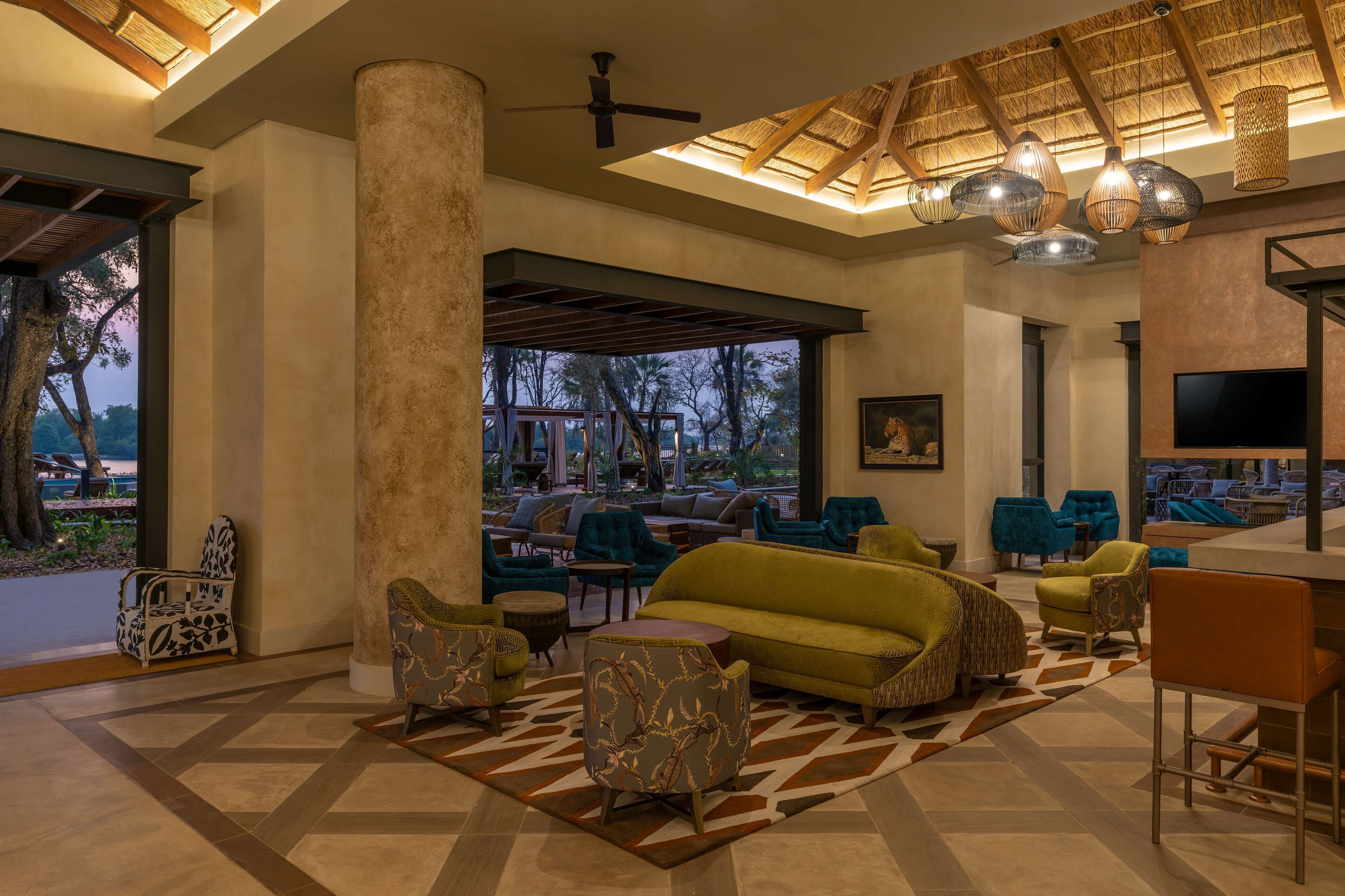 A spacious lobby with a large column, a green sofa, and multiple chairs. There is a ceiling fan and hanging lamps.