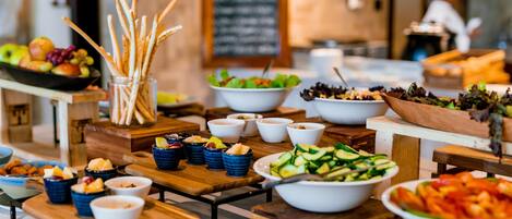 A buffet setup with various bowls of food, including salads, fruits, and snacks, arranged on wooden tables.