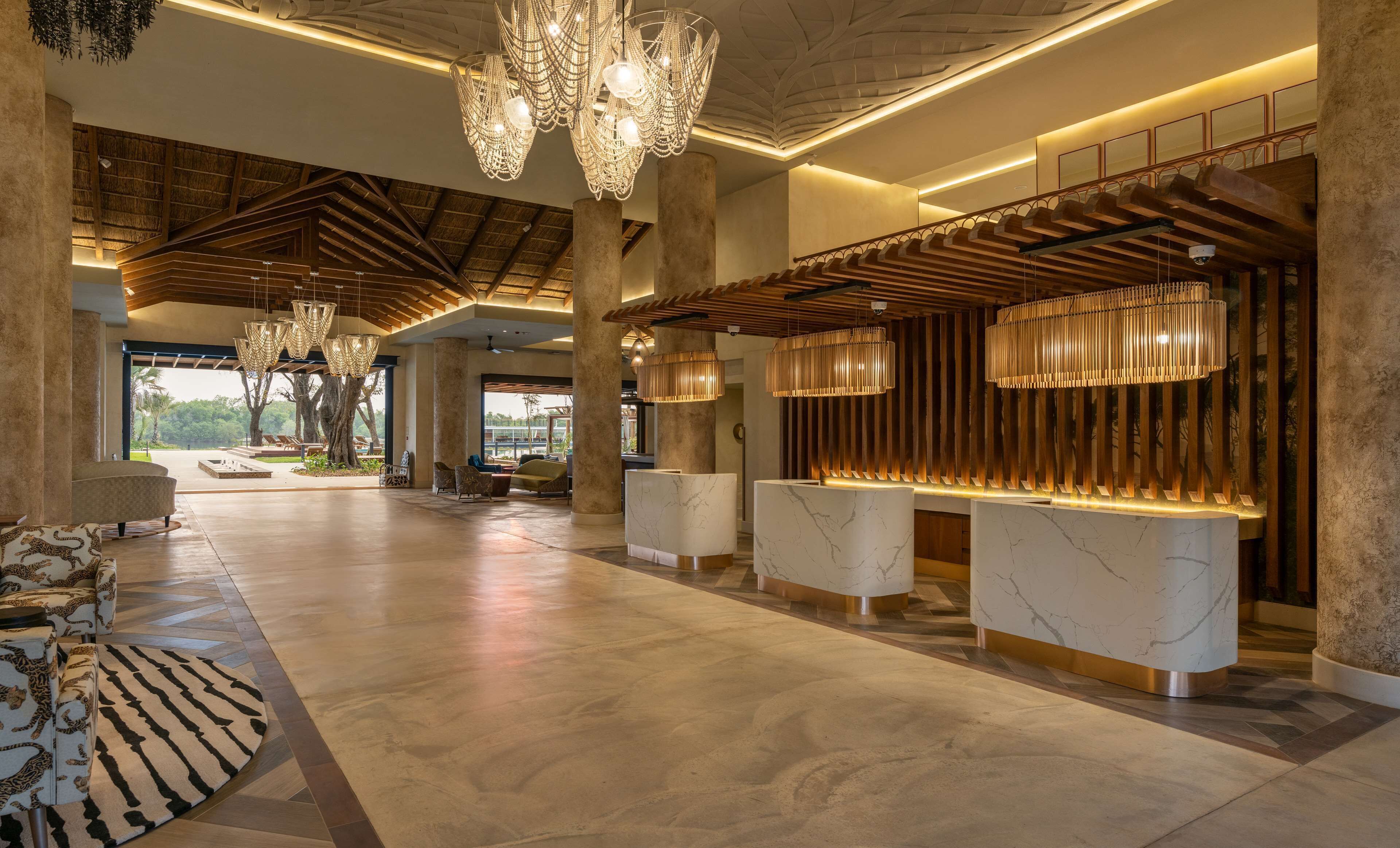 A spacious lobby with a high ceiling, large chandeliers, and a reception desk with marble counters.