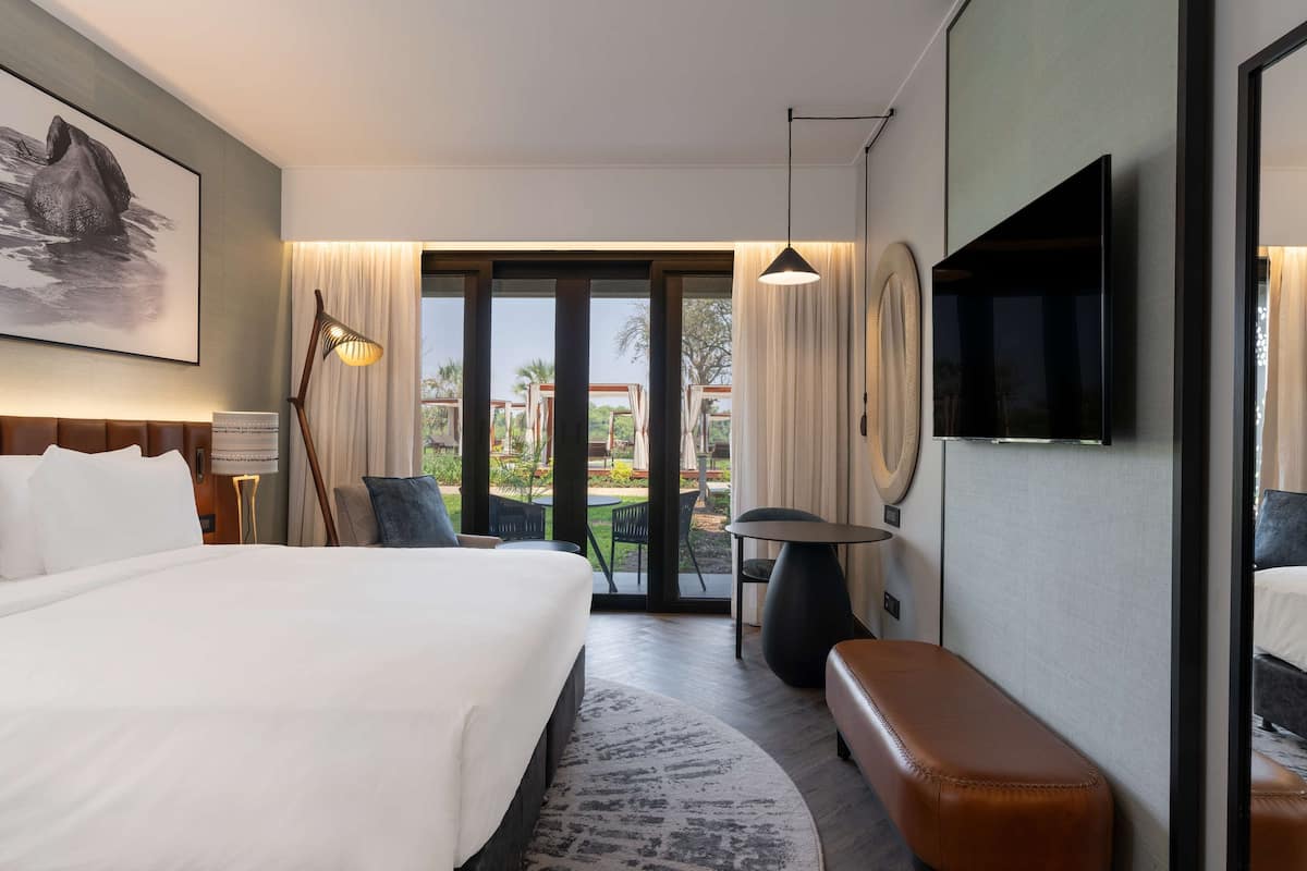 Une chambre d’hôtel avec un grand lit, un bureau, une chaise, un banc, une télévision et une vue sur l’extérieur.