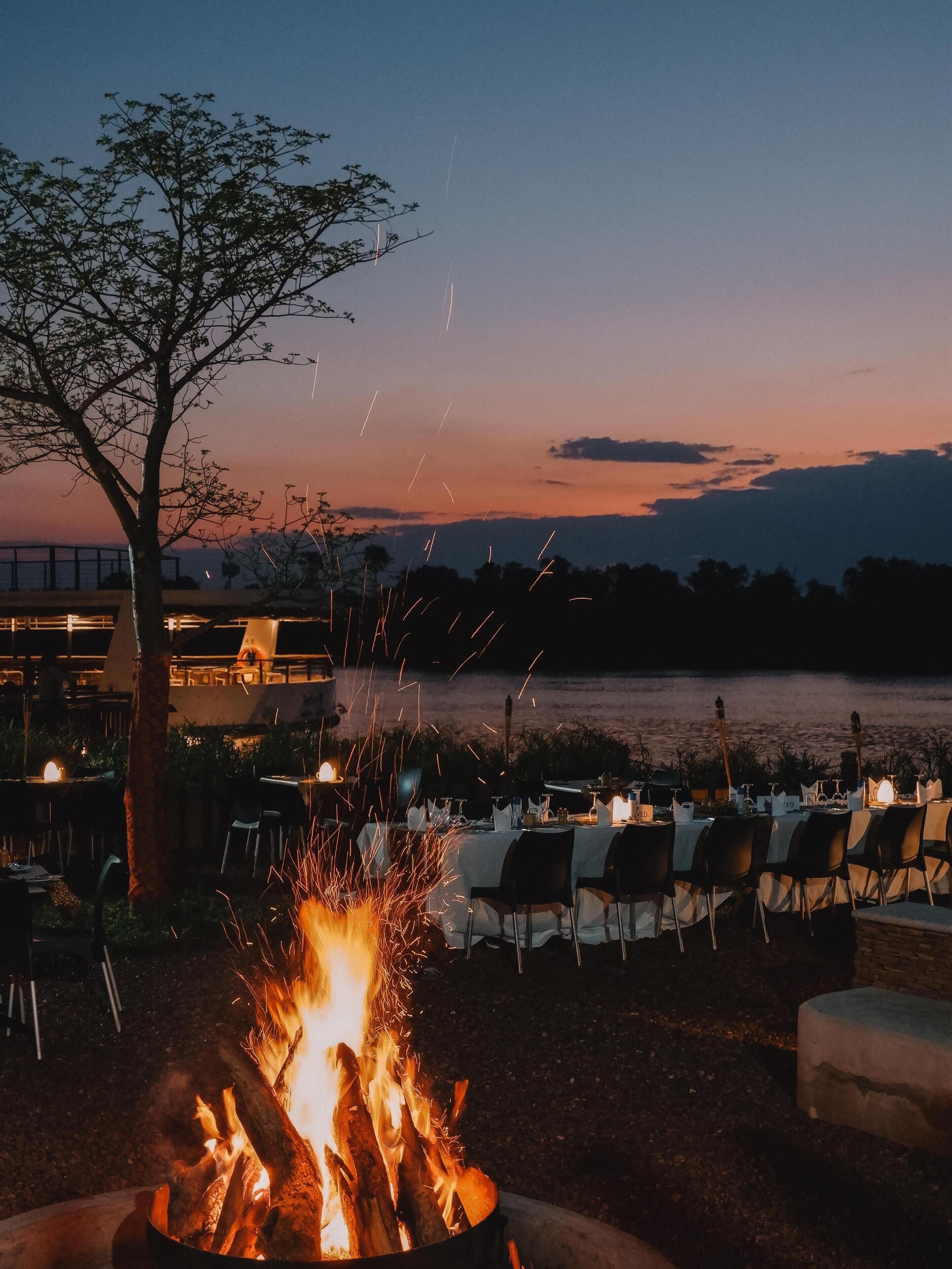 Un espacio al aire libre con mesas y sillas, una chimenea y vistas al agua y al cielo.