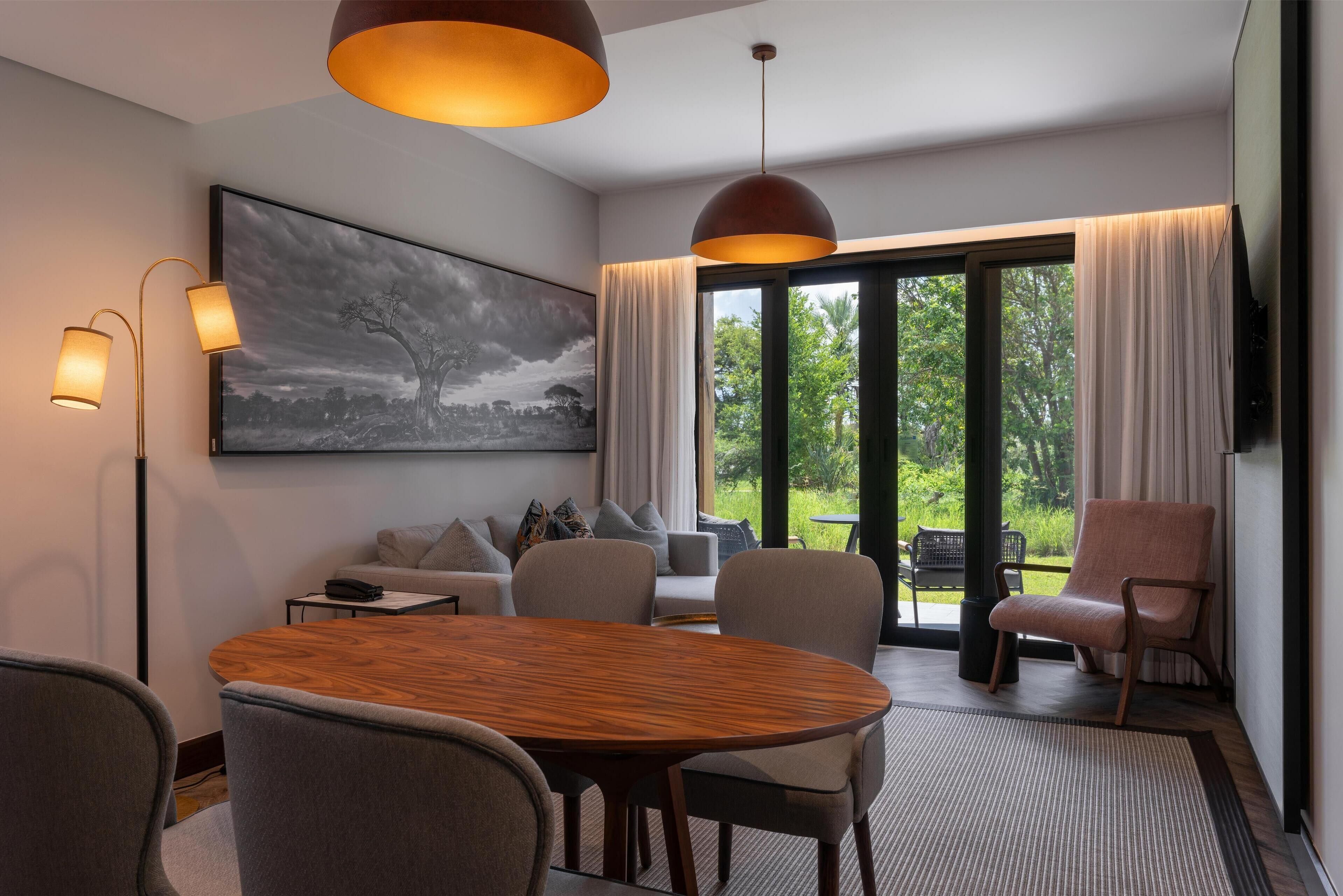 A modern hotel room with a large window, a round wooden table, and a comfortable seating area.