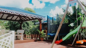 An outdoor patio with a covered seating area, a trampoline, and a swing set. - Le Lodge Phoenix, F2 in residence with swimming pool (Sainte-Rose)