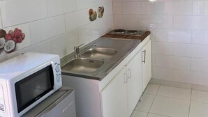 A compact kitchen with white cabinets, a green upper cabinet, a microwave, a refrigerator, and a sink. - Le Lodge Phoenix, F2 in residence with swimming pool (Sainte-Rose)