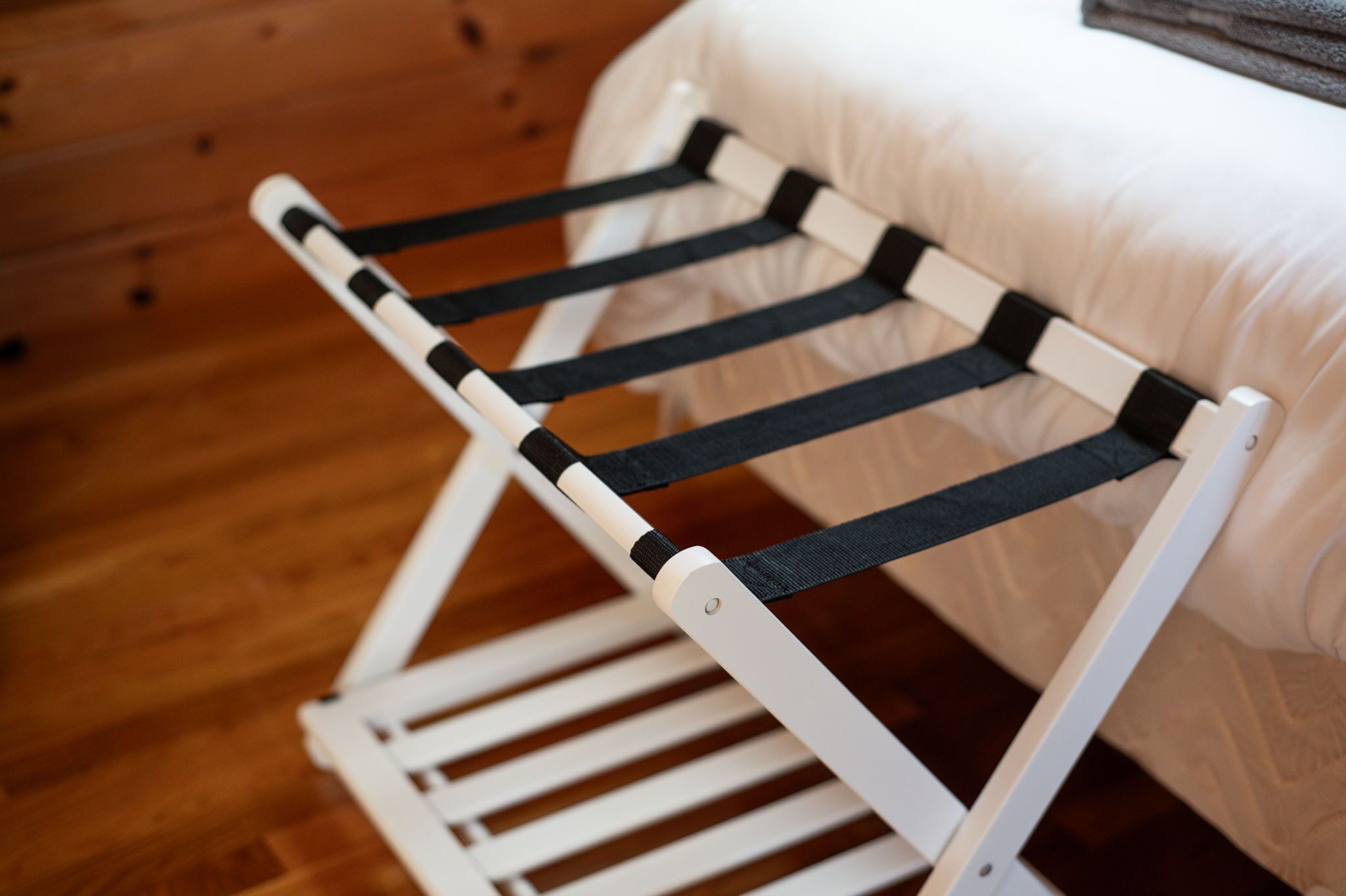 A white metal rack with black straps, likely for hanging items, positioned against a wooden wall and a white cushioned surface.