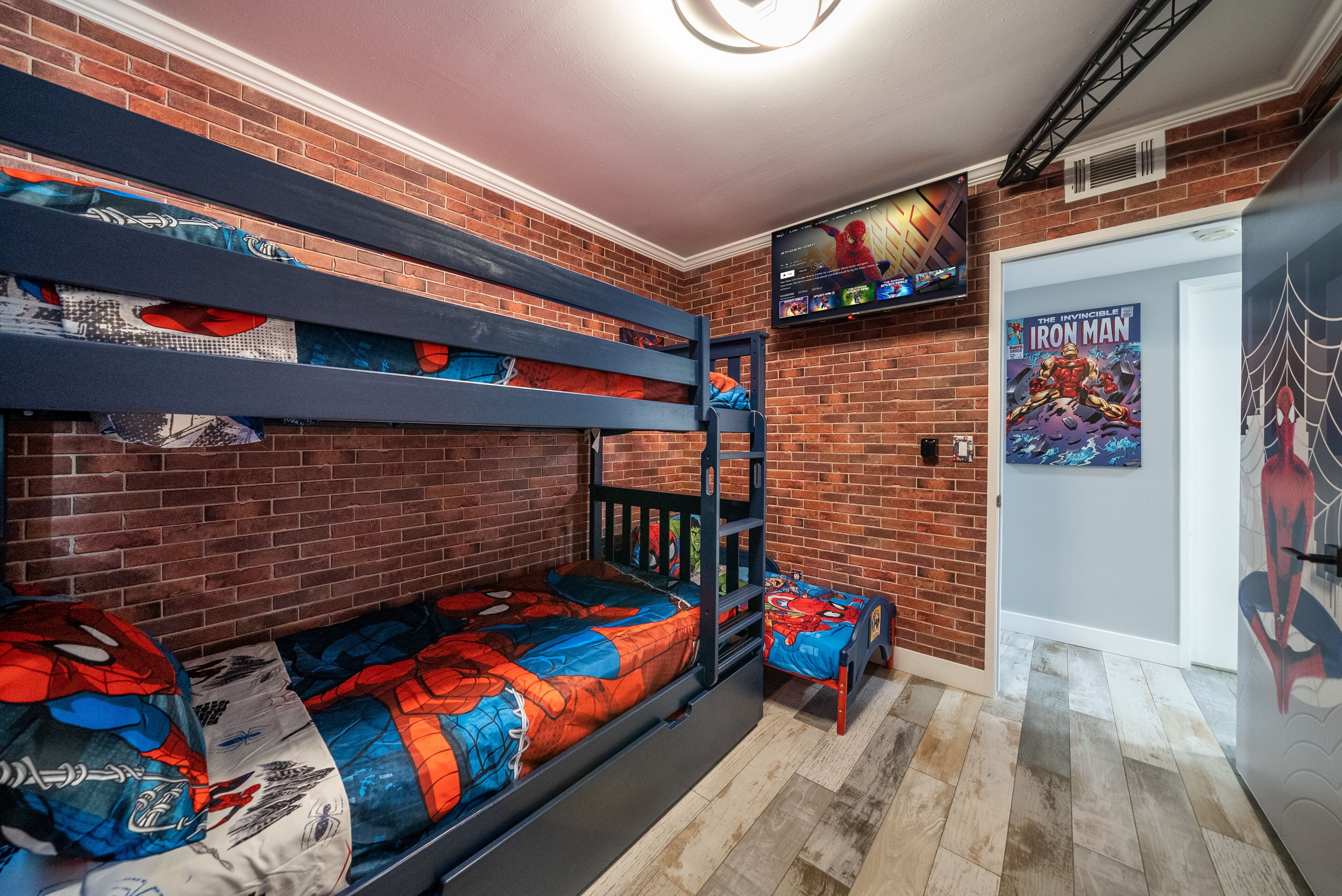 A room with a bunk bed, a TV mounted on the wall, and a Spider-Man poster.