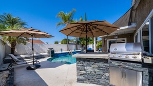 A backyard with a swimming pool, two umbrellas, a barbecue grill, and a stone wall. - Avengers Campus: 🌊🎥🍿🕹Heated Pool, Theater, Arcade+ (Stanton)