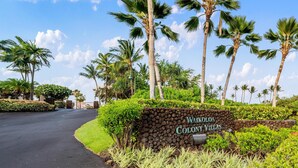 Schild für die Waikoloa Colony Villas mit befestigter Straße und Palmen.
