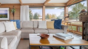 A modern living room with a large sectional sofa, a wooden coffee table, and a view of the outdoors through large windows.