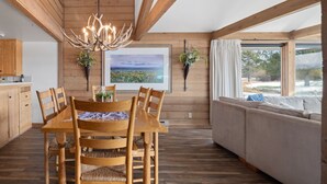 A wooden interior with a dining table, chairs, a chandelier, a sofa, and a view of the outdoors.