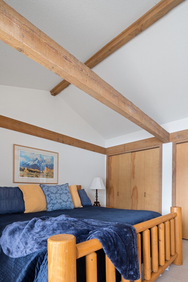 A bedroom with a wooden bed frame, a blue blanket, and a mountain painting on the wall.