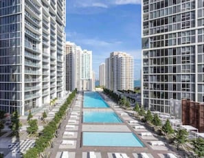 A high-rise residential building with multiple balconies, a central swimming pool, and a clear sky.