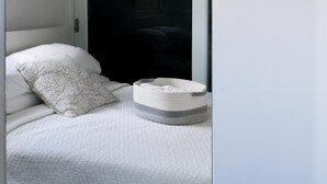 A bed with a white quilted mattress, a white pillow with a leaf pattern, and a grey and white woven basket.