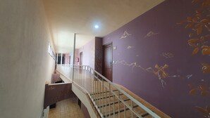 A hallway with a purple wall, a staircase with a metal railing, and a door at the end. - Posada Los Pedregales (El Granado)