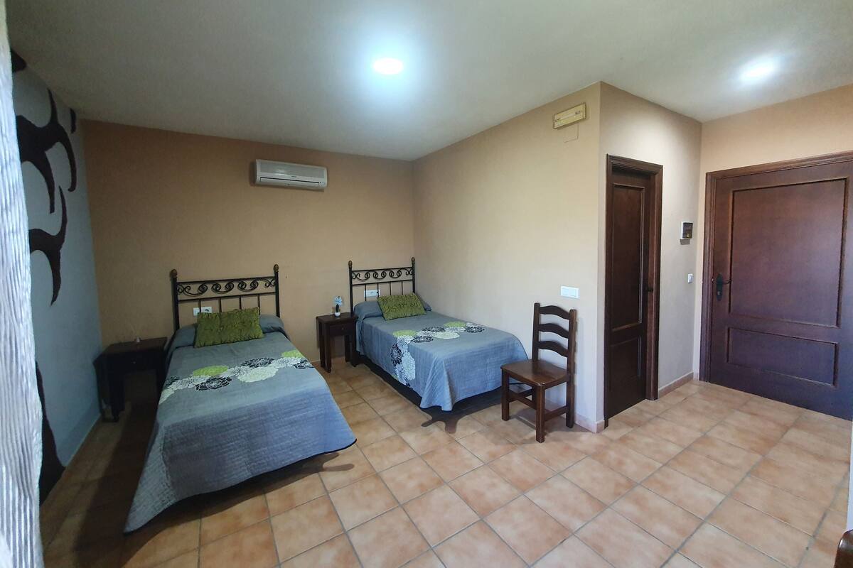 A room with two beds, a chair, a door, and an air conditioning unit.