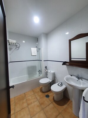 Een badkamer met een bad, twee toiletten, een wastafel en een douche.