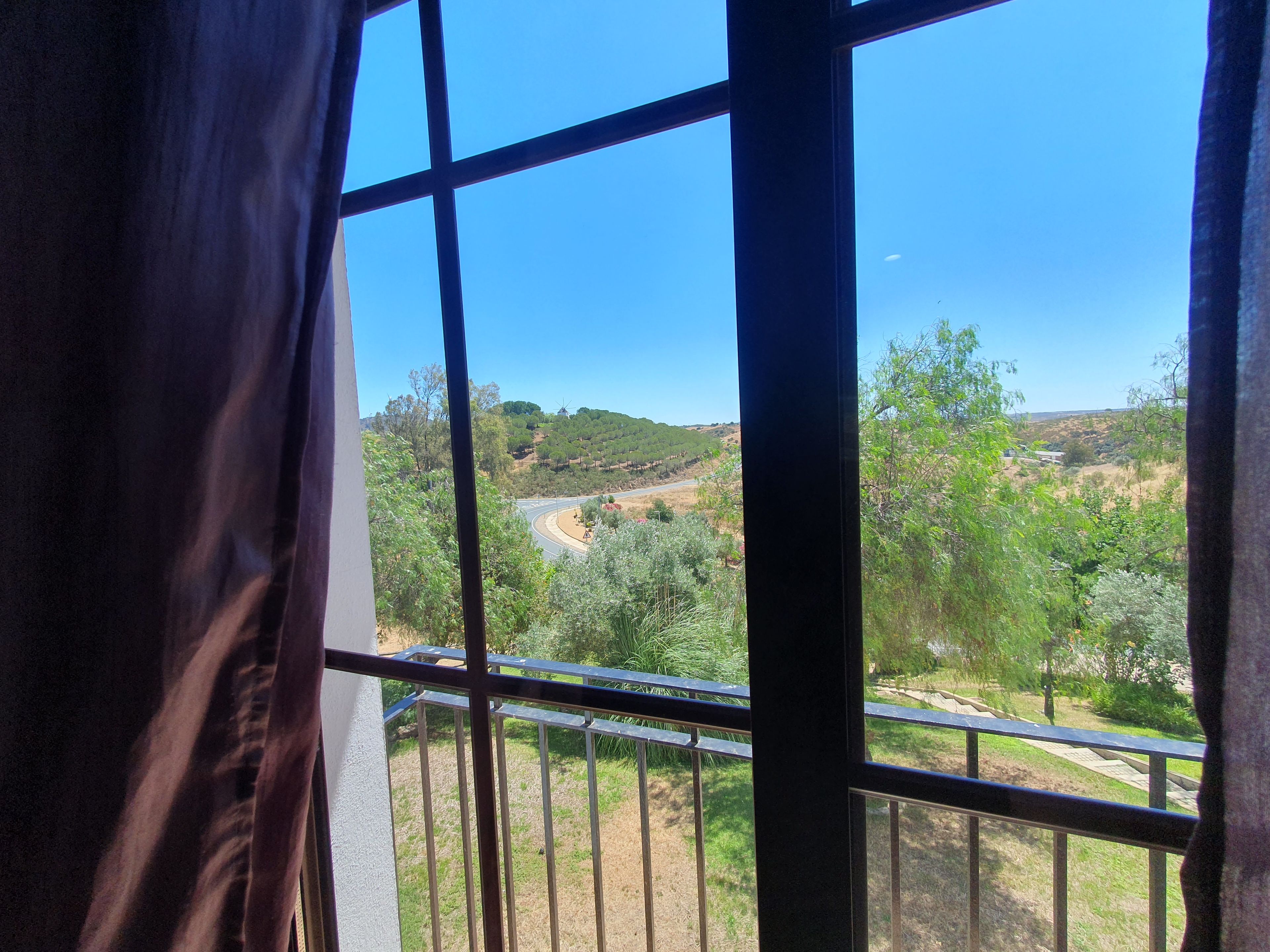 Vista a través de una ventana con barrotes, mostrando un paisaje con vegetación, colinas y una carretera.