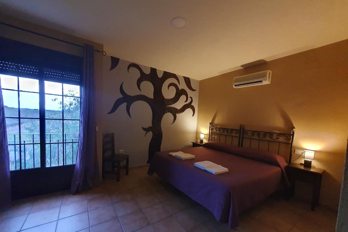 A bedroom with a bed, a chair, a wall mural, an air conditioner, and a window with curtains.