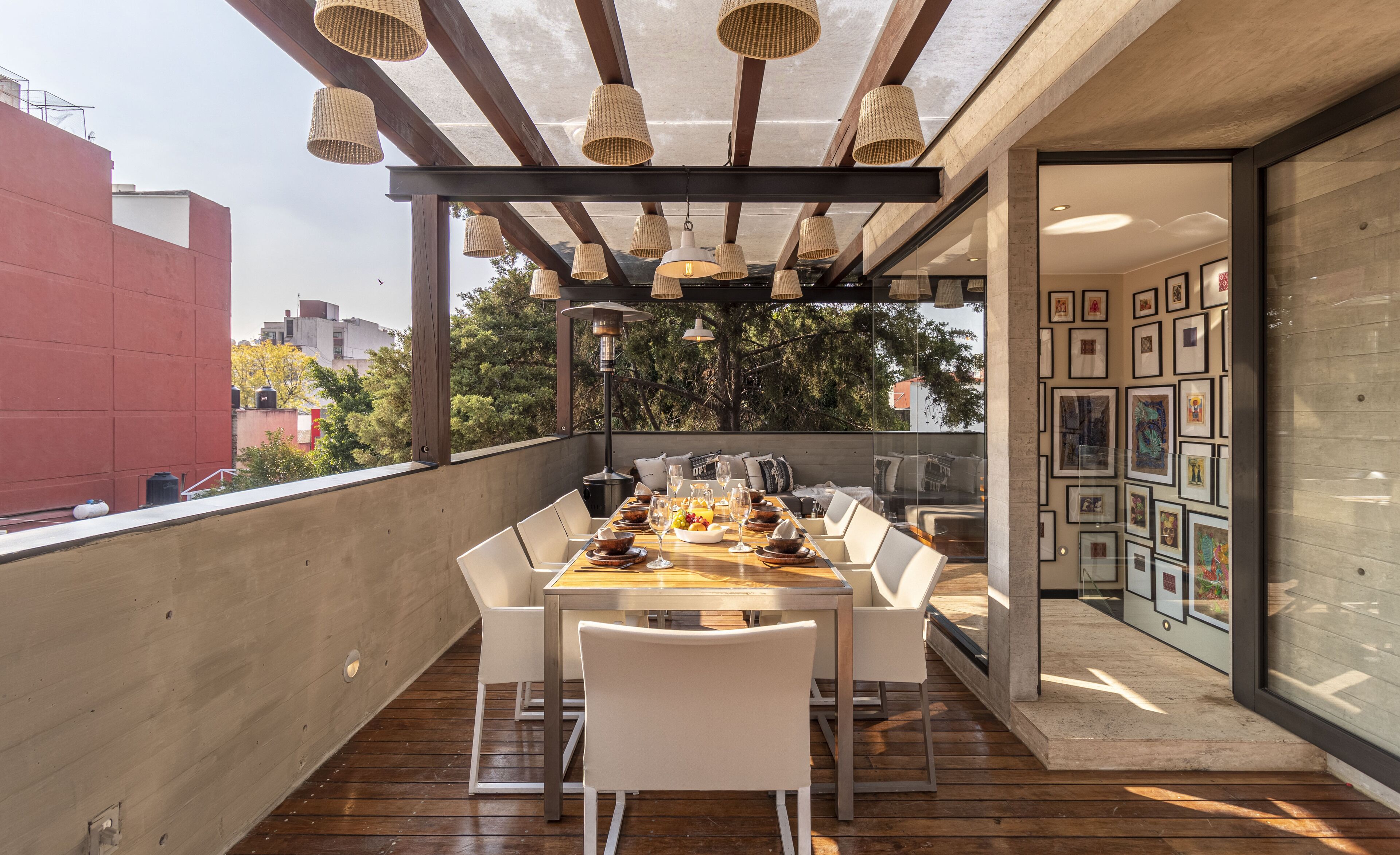 Un espace de restauration en plein air avec une table en bois, des chaises blanches et des lampes en osier suspendues.