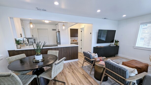 A modern living room with a dining area, wooden flooring, and a large TV.