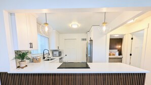 A modern kitchen with white cabinetry, a central island, a microwave, and a refrigerator.