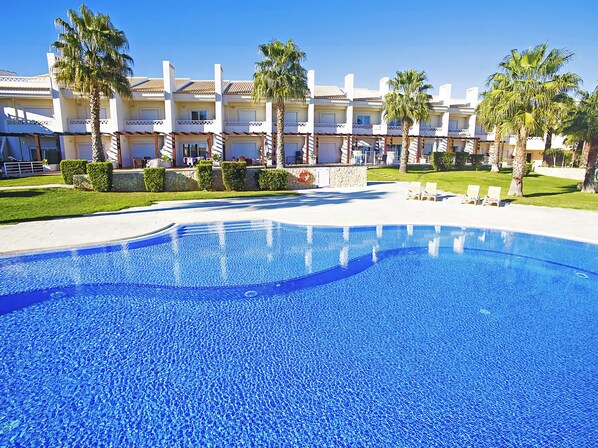 A swimming pool with a clear blue water surface, surrounded by a well-maintained lawn and palm trees.