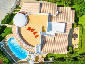 An aerial view of a resort with a swimming pool, sun loungers, and a covered outdoor seating area.