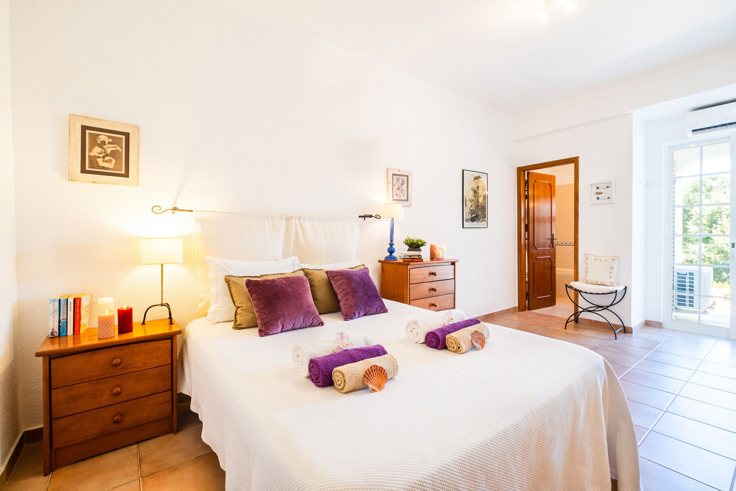 Une chambre d’hôtel comprenant un lit, des tables de chevet, une commode, une chaise et une porte donnant sur un balcon.