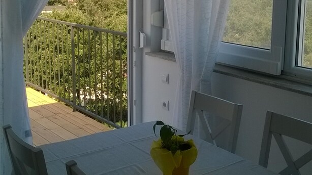 A dining area with a table set for two, a yellow flower vase, and a view of the sea through a window with white curtains. - Apartment in Zaton (Zadar) with Seaview, Balcony, Air condition, WIFI (685-2) (Nin)