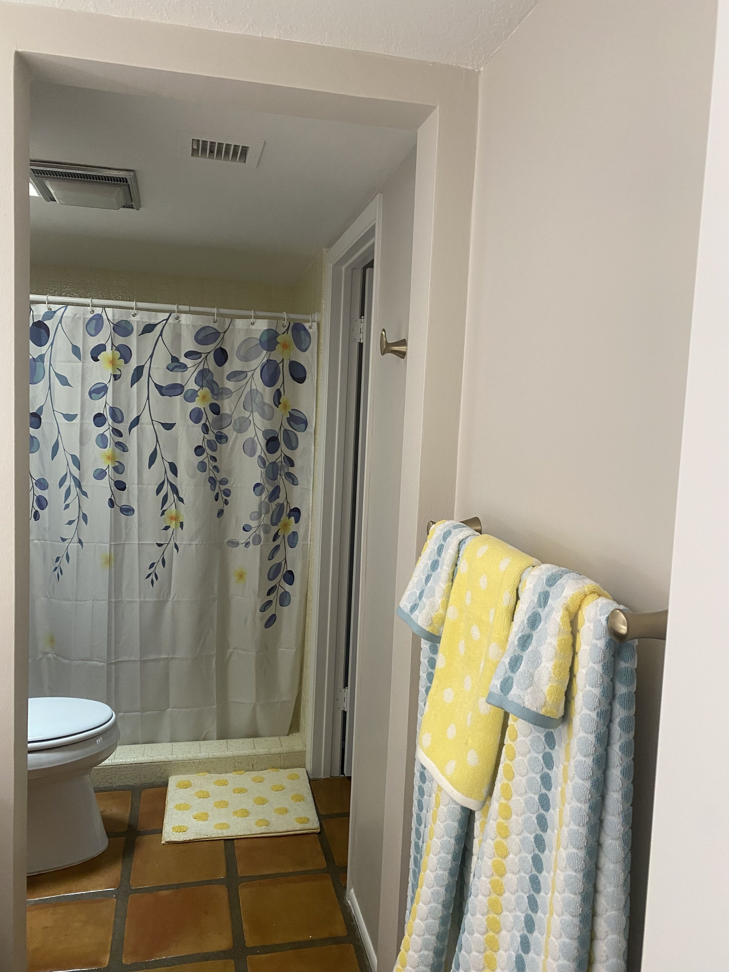 A bathroom with a toilet, a shower curtain with a floral pattern, and a towel rack with towels.