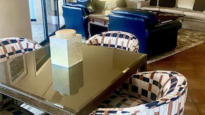 Un salon moderne avec une table basse en verre, des fauteuils à carreaux bleus et blancs, un canapé blanc et un téléviseur à écran plat fixé au mur.