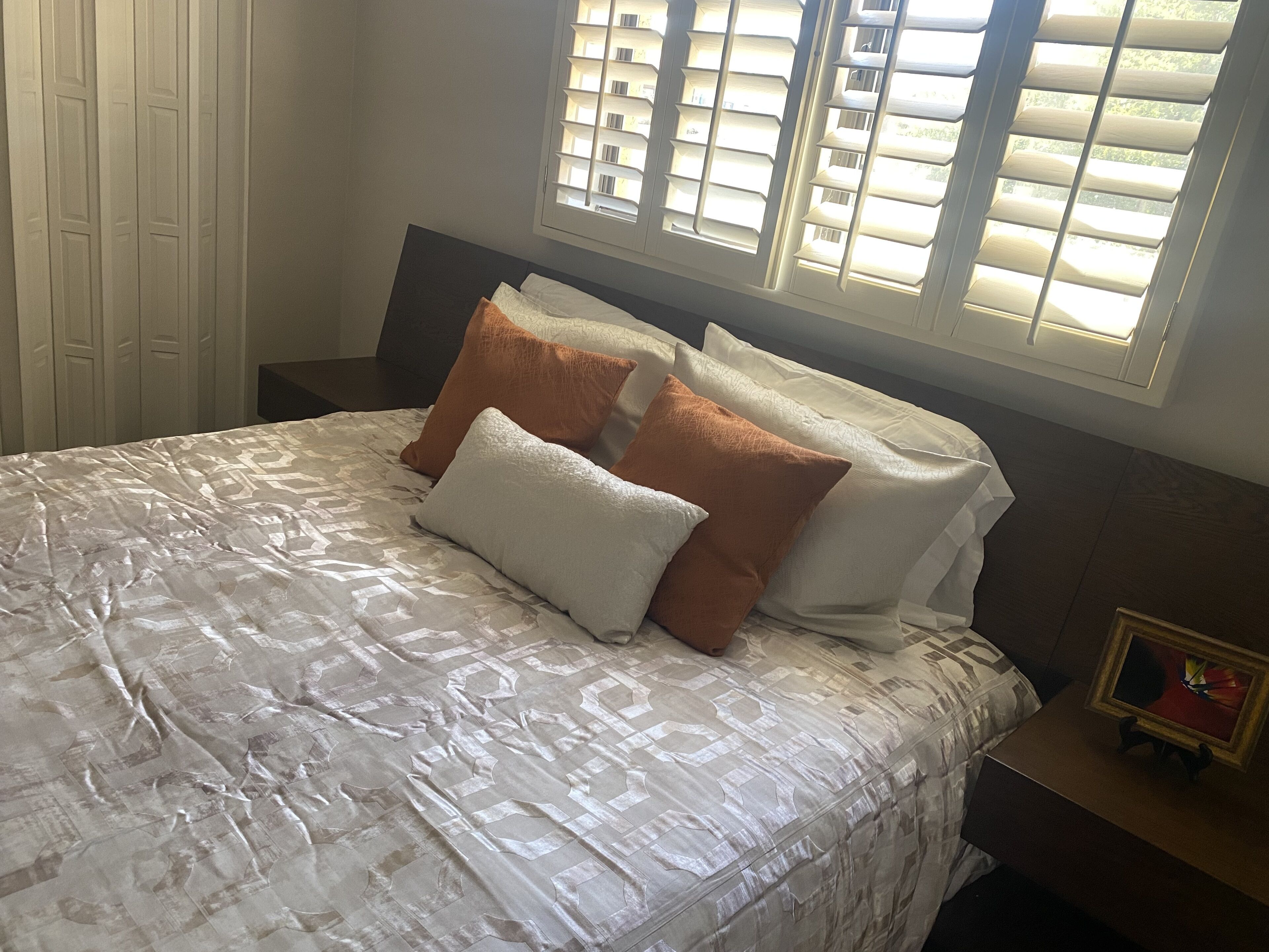 Een net opgemaakt bed met een bedsprei met dessin, twee kussens en een nachtkastje met een ingelijste foto.