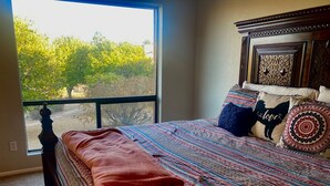 Une chambre avec une grande fenêtre, une couvre-lit à motifs et une vue sur les arbres à l’extérieur.