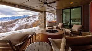 A covered outdoor seating area with a fire pit, stone pillar, and a view of mountains.