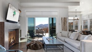 A modern living room with a fireplace, a sofa, a coffee table, and a view of mountains through large sliding doors.