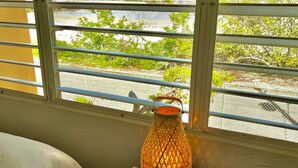 Una habitación con una cama, una mesita de noche con lámpara y una ventana que da a vistas de vegetación y una valla.
