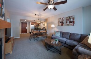 A modern living room with a sofa, coffee table, and dining area. There is a ceiling fan, artwork on the wall, and a fireplace. - Ski Condo with Mountain and Resort View - Fraser Crossing/Founders Pointe Select-Rated 4457 (Winter Park)