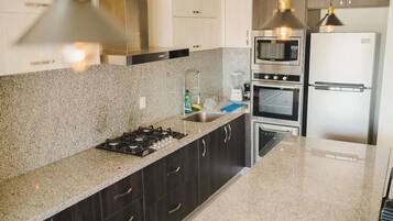 Una cocina moderna con armarios oscuros, encimera de granito, estufa a gas, horno, microondas y refrigerador.