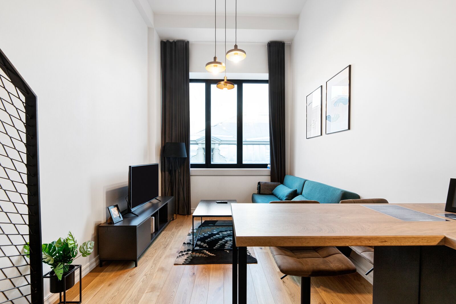 Una sala moderna con una mesa de comedor de madera, un sofá, un televisor y un amplio ventanal con cortinas.