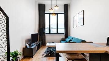 Una sala moderna con una mesa de comedor de madera, un sofá, un televisor y un amplio ventanal con cortinas.