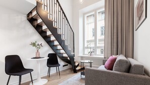 A modern living room with a staircase, a grey sofa, black chairs, a small table, and a window with curtains. - Bob W Tartu Old Town (Tartu)