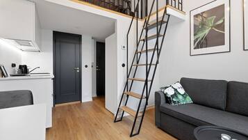 Un apartamento moderno con cocina, un sofá gris, una escalera y una planta enmarcada en la pared.