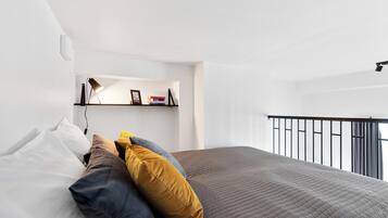A modern bedroom with a bed, pillows, a shelf with books, and a balcony railing.