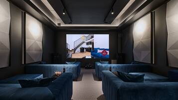 A modern, dark-themed living room with a large screen displaying a room. There are plush blue sofas and a patterned carpet.