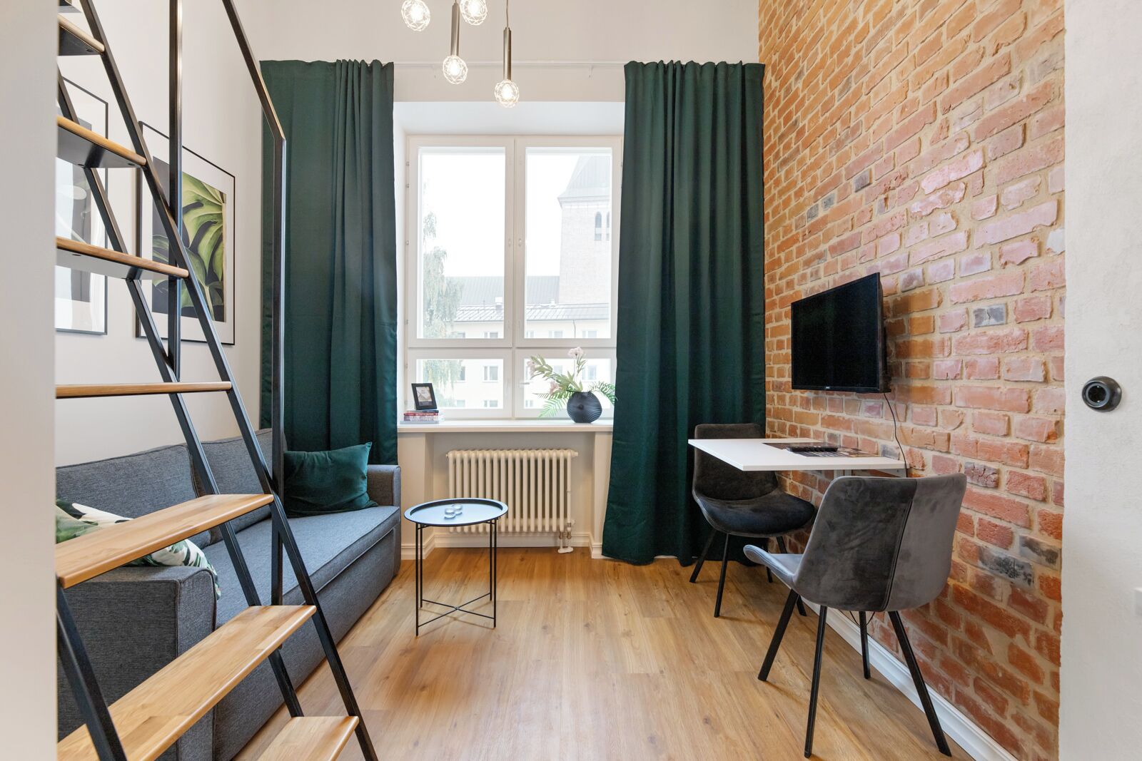 Un espacio habitable moderno con una escalera, un sofá, una mesita y un televisor instalado en una pared de ladrillo.